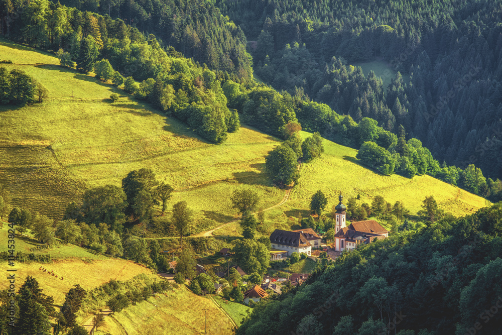 Scenic countryside landscape: summer mountain valley with forests, fields and old church in Germany, Black Forest