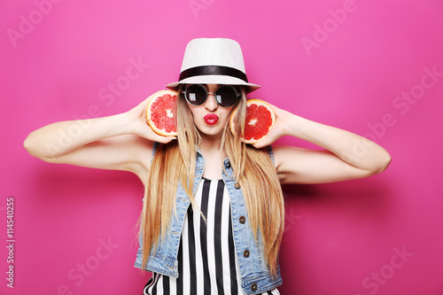 Portrait of a beautiful hipster girl with grapefruit on pink bac