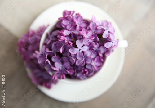 Purple lilac flowers in a cup on wooden table