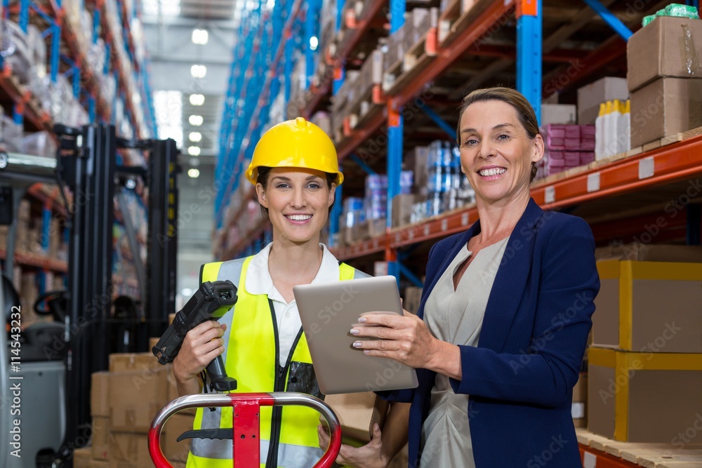 Businesswoman and warehouse worker looking at camera Businesswoman and warehouse worker looking at camera