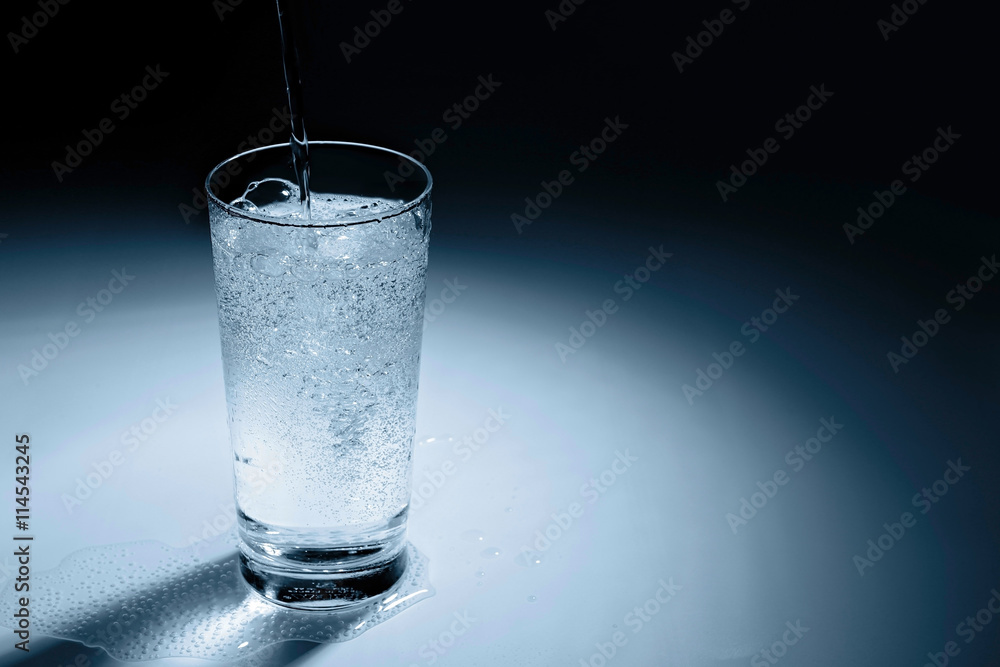 Pouring water into glass on blue background Pouring water into glass on blue background