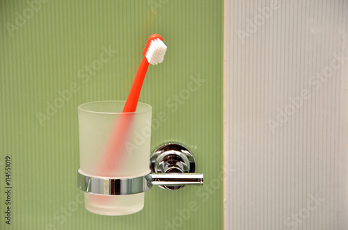 Toothbrush in glass in metal holder fixed to green tile at wall in bathroom