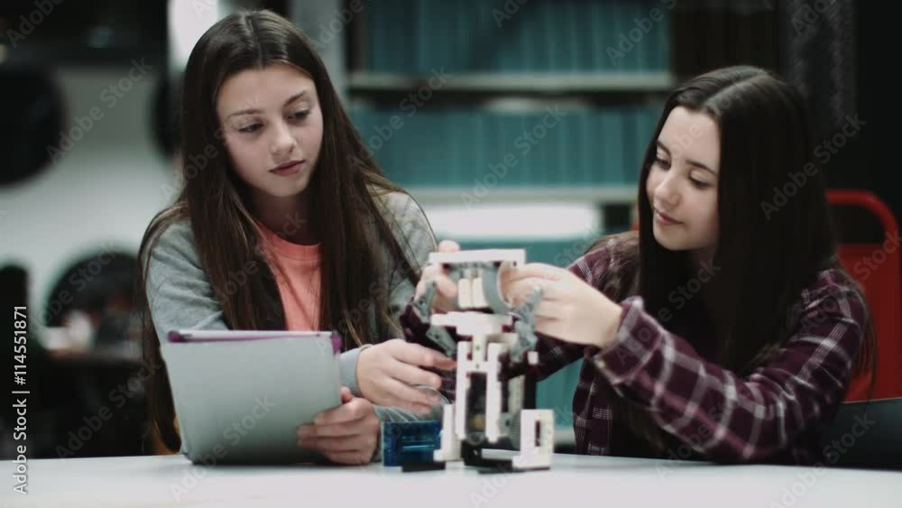 Teenage girls working with digital tablet and robot in library Teenage girls working with digital tablet and robot in library