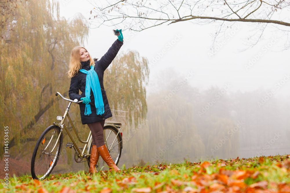 Obraz premium Happy woman with bike in park taking selfie photo.