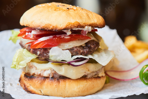 A hamburger consisting of meat patties, cheese and vegetables close up