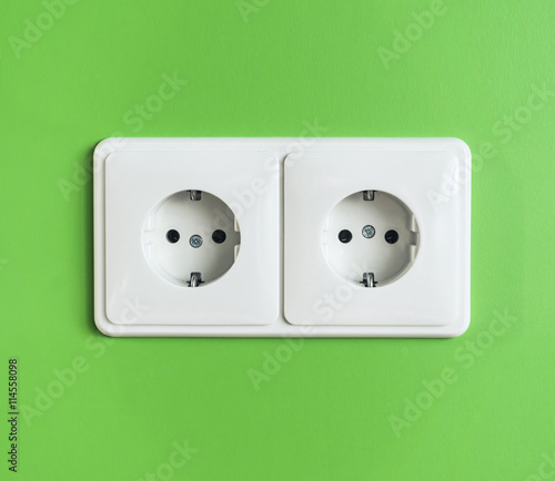 Two white electrical power sockets on a green wall