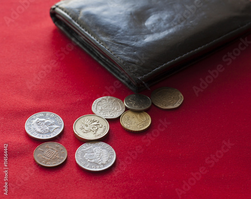 Pounds and euro coins lying on red background with black leather wallet photo