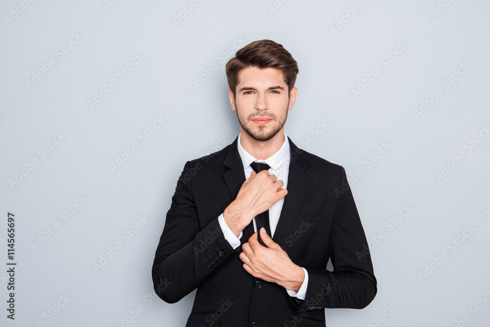 Portrait of handsome businessman correcting tie on gray backgrou Portrait of handsome businessman correcting tie on gray backgrou