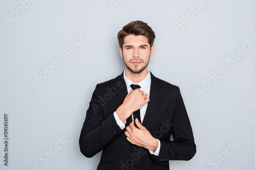 Portrait of handsome businessman correcting tie on gray backgrou