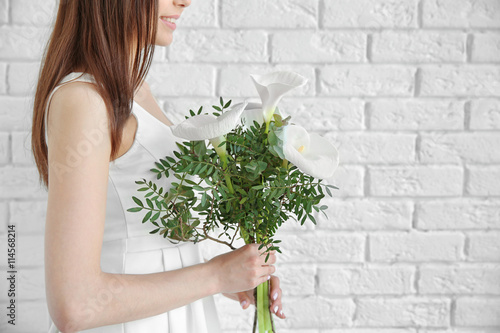 Beautiful young woman holding bouquet of callas on white brick wall background