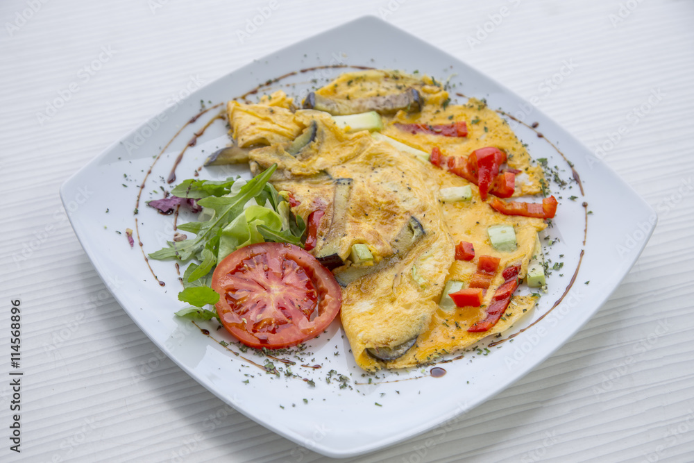 Omlette with herbs,vegetables and cheese in a plate on wooden table. Omlette with herbs,vegetables and cheese in a plate on wooden table.