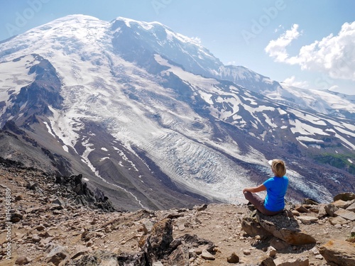 Woman in yoga pose meditating with ice covered mountain view. Burroughs Mountain Trail, Mount Rainier National Park, Seattle,  Washington, USA. photo