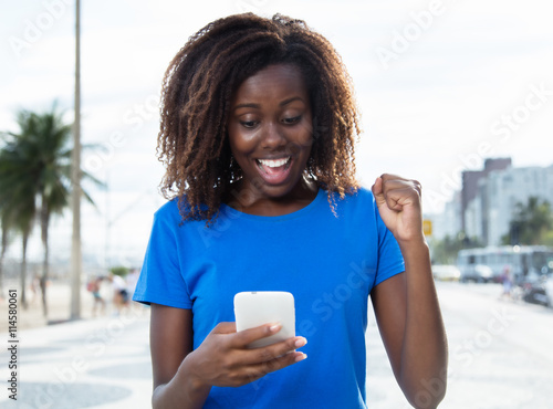 Cheering african woman in a blue shirt with phone photo