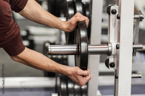 Male hand putting weight plate on barbell. Weightlifting training preparation. Weight plate in strong hand of fitness instructor in gym closeup