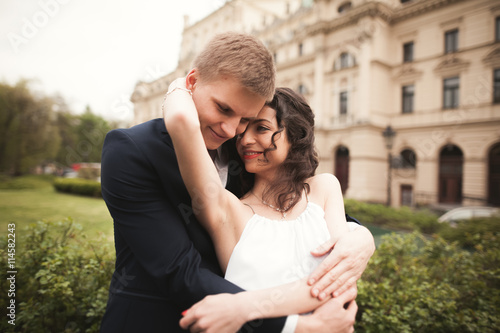 Beautiful wedding couple, bride, groom kissing and hugging against the background of theater © olegparylyak