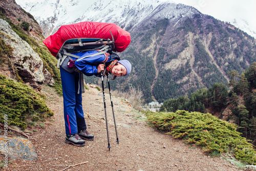 hiking woman with backpack have a rest on a trail with her trekking poles on the background of high Caucasus mountains