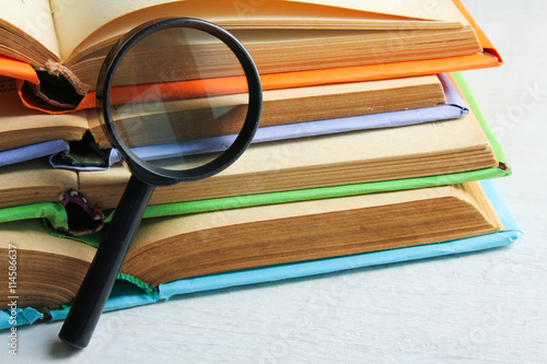 books in colorful covers and pads near a magnifying glass on white wooden table