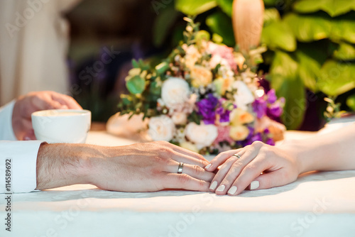 Man and woman s hands with espousal rings  coffee  wedding. Closeup of bride and groom holding hands in cafe. Wedding rings on their fingers.