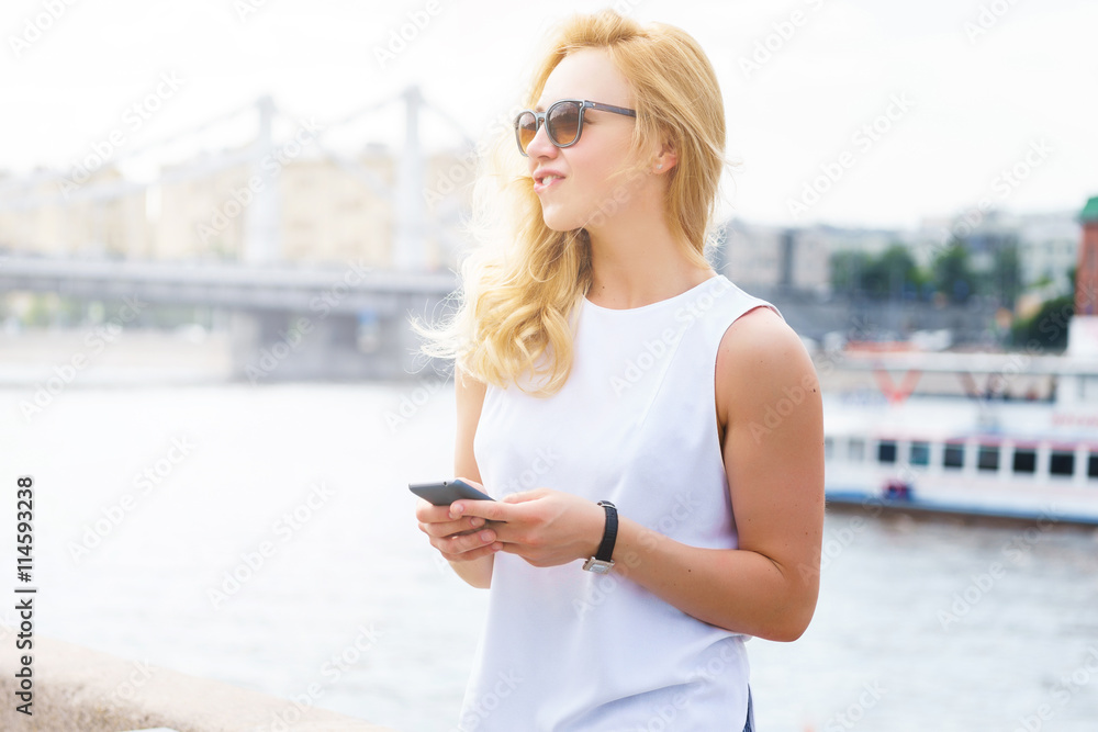 Casual woman in sunglasses with blonde hair keeps smart-phone