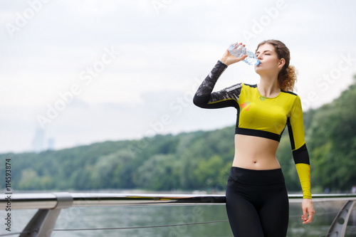 Sporty woman drinking water after training