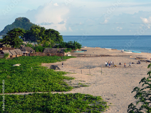 Fin de journée sur la plage d'un village africain des Comores. Les barques de pêche sont renversées sur le sable, quelques personnes discutent, à l'arrière-plan les premières maisons du village