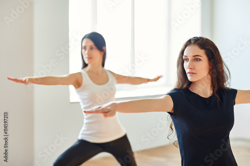 Two young women doing yoga asana Virabhadrasan