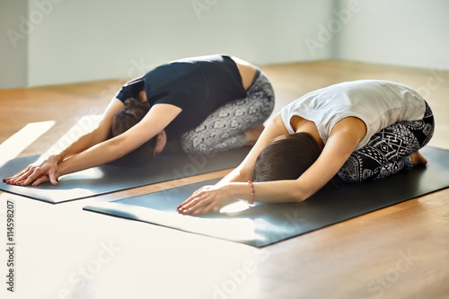 Two young women doing yoga asana child's pose