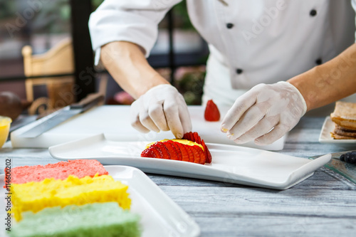 Hands touch slices of strawberry. Plate with pieces of berry. Flan with fresh strawberry. Pastry chef at work.