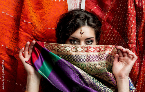 The young dark-haired woman hides a face behind a piece of colorful Indian saris. Indian style.