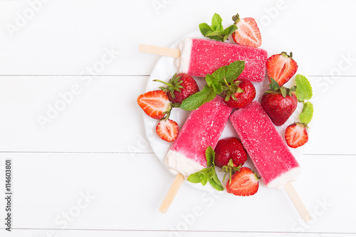 Frosty strawberry popsicles on a plate with mint on a white wooden background. Top view with copyspace
