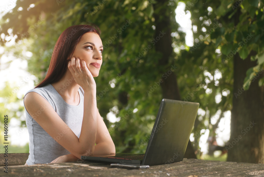 Beautiful young woman sitting in the park, using a laptop, thinking Beautiful young woman sitting in the park, using a laptop, thinking