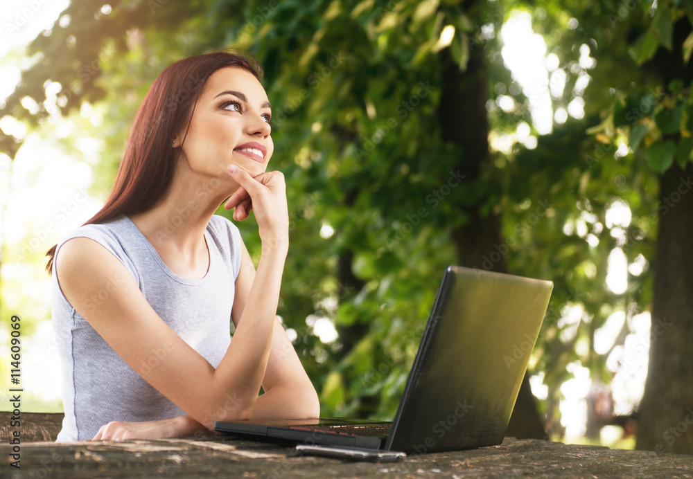 Beautiful young woman sitting in the park, using a laptop, thinking Beautiful young woman sitting in the park, using a laptop, thinking