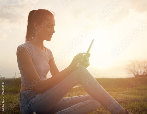 Beautiful young woman sitting outdoors, using a tablet