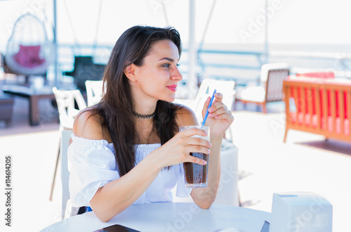 Woman sitting in cafe with ice coffee with sky and sea background. Selective focus.