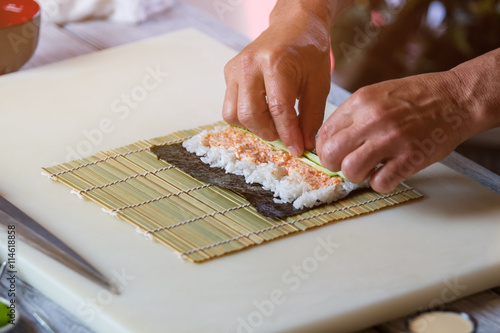 Man's hands touch cucumber slices. Nori leaf on bamboo mat. Recipe from japanese chef. Preparation of makizushi.