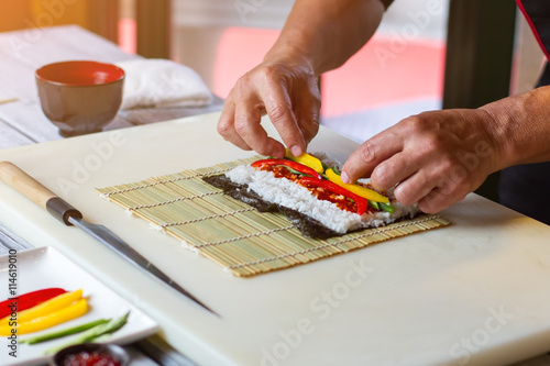 Hands touch pieces of paprika. Sliced bell pepper on rice. Sushi ingredients on bamboo mat. First lesson in cooking school.