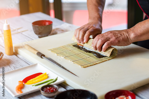 Man's hands touching bamboo mat. Knife lying near bamboo mat. Sushi chef in restaurant kitchen. Old recipe of futomaki rolls.