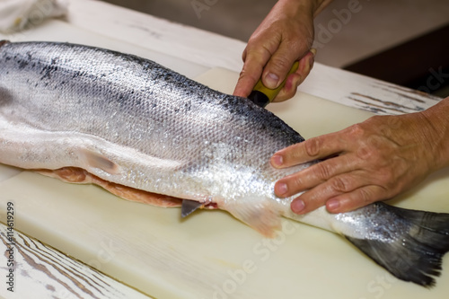 Kitchen knife cuts raw fish. Man's hand on raw fish. Kitchen table in sushi bar. Salmon meat required for recipe.