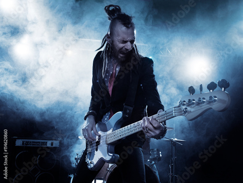 Rock band performs on stage. Bassist in the foreground. Close-up.