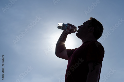 Mann trinkt Mineralwasser aus Flasche im Gegenlicht