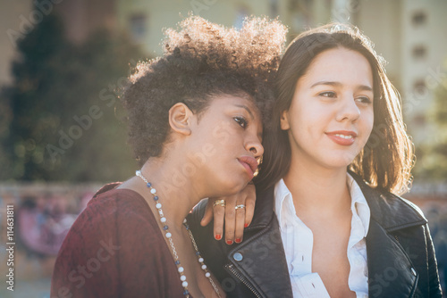 Half length of two young multiethnic friends outdoor in the city back light, overlooking - friendship, woman power, serenity concept