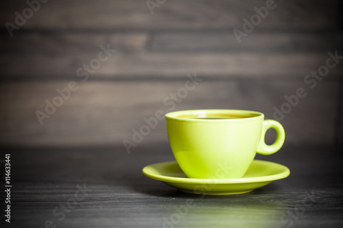 Green cup of hot tea on wood background with leaf. Autumn.
