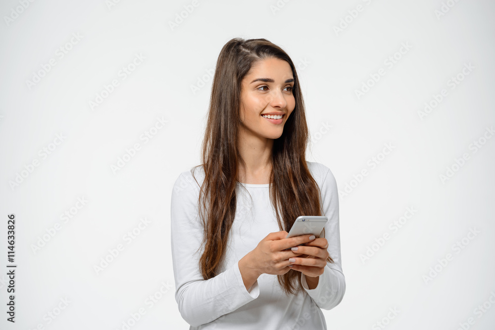 Portrait of young happy girl holding her phone in hand looking aside over white background Portrait of young happy girl holding her phone in hand looking aside over white background