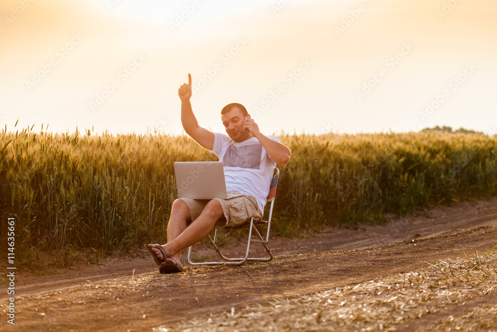 Businessman sitting in the field and working on laptop.