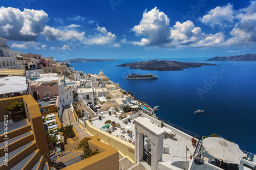Greece. Santorini (Thira). Fira town with characteristic style for Cycladic architecture - white-washed cube houses built on the edge of high cliff. There is Nea Kameni Island in the background
