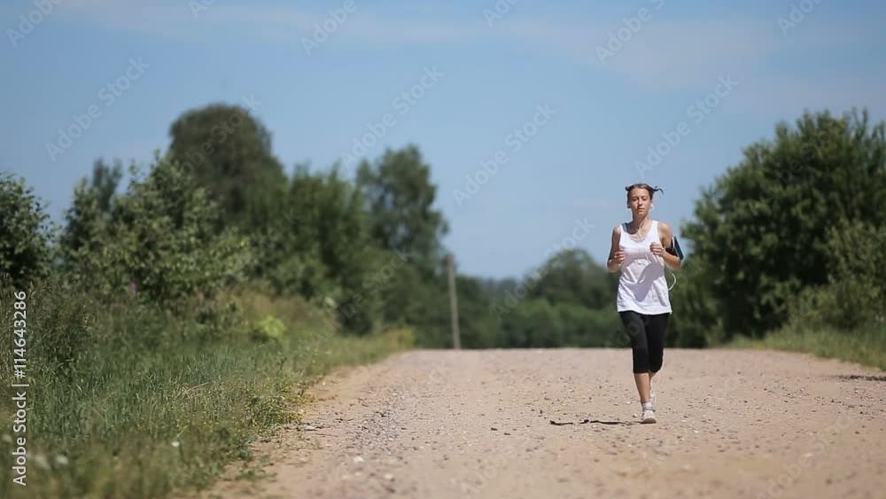 Beautiful teenage girl running on the road on sunny summer day.Young beautiful girl running and listening to music with headphones. Beautiful teenage girl running on the road on sunny summer day.Young beautiful girl running and listening to music with headphones.