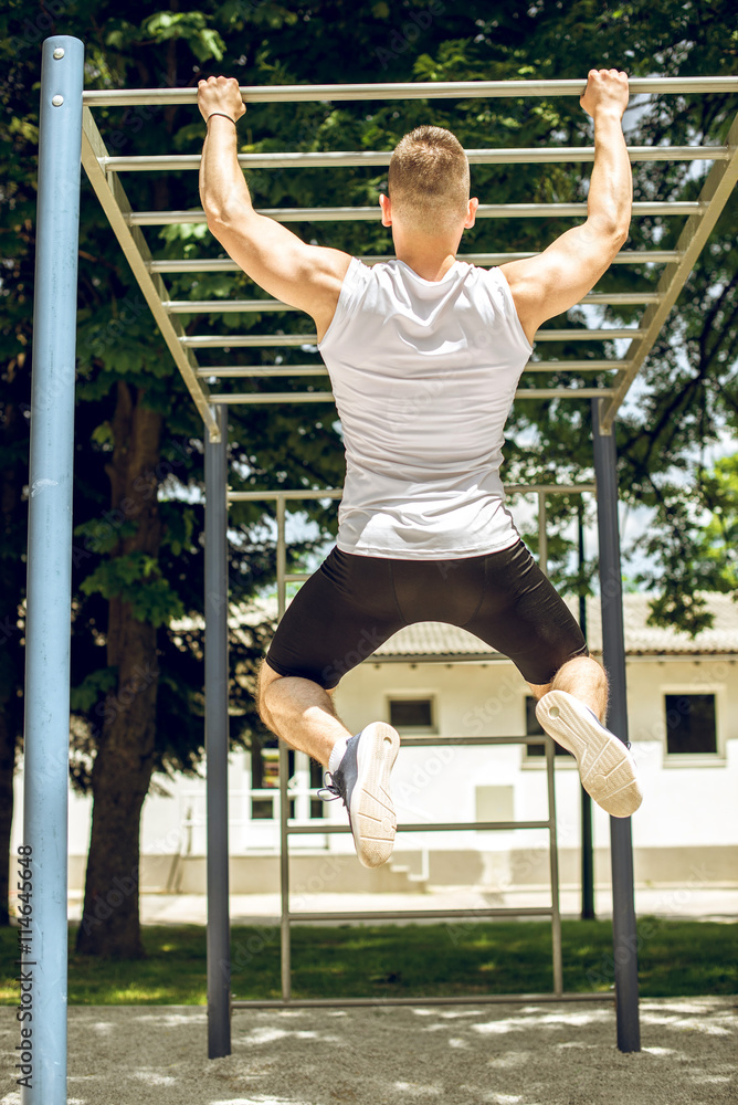 Muscular man doing pull-ups exercise outdoors.