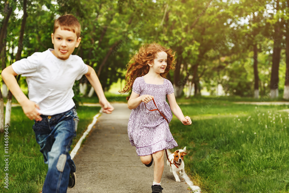 Boy and girl run in a park with a puppy jack russell terrier.