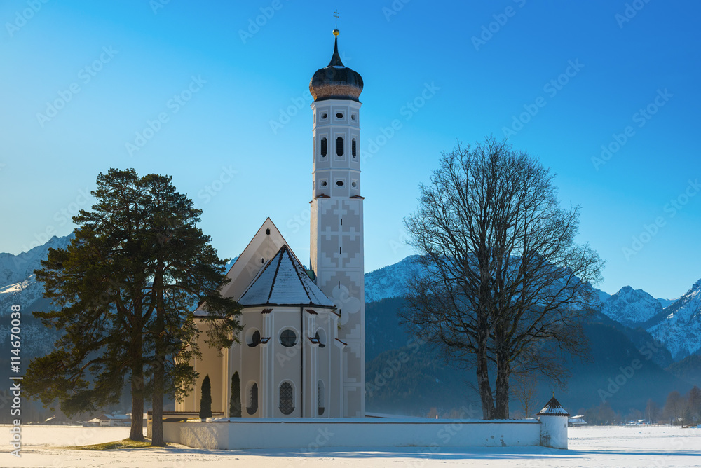 A sunny view of St. Coloman church in winter with snow cover and blue sky