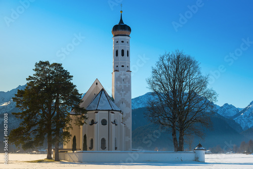 A sunny view of St. Coloman church in winter with snow cover and blue sky